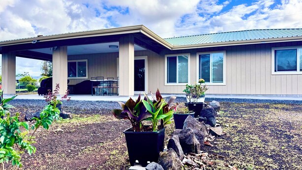 Uma casa moderna com um alpendre coberto, área de estar externa e um jardim ajardinado com vasos de plantas e pedras.