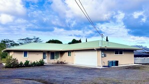 Uma casa térrea com telhado verde, revestimento bege e garagem.