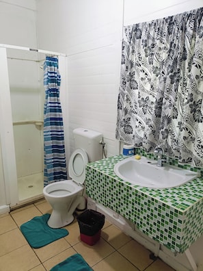 A bathroom with a toilet, a sink, a shower curtain, and a tiled floor. - Olivias Accommodation (Apia)