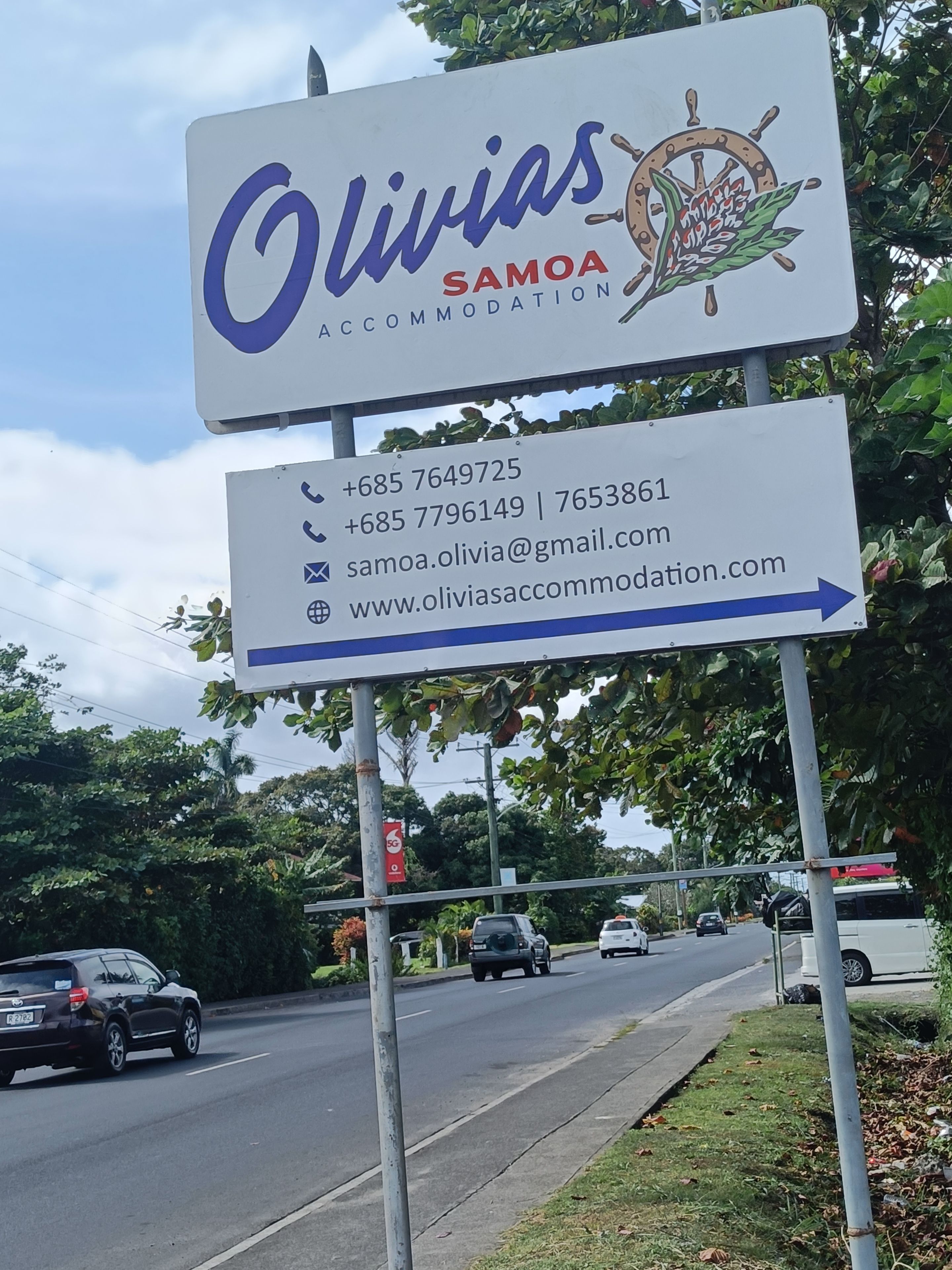 Un letrero de Olivia's Samoa Accommodation con datos de contacto y una flecha indicativa.