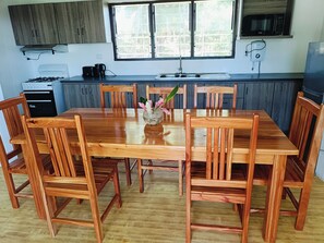 Una mesa de comedor de madera con sillas, un florero con flores y una cocina con armarios y electrodomésticos.