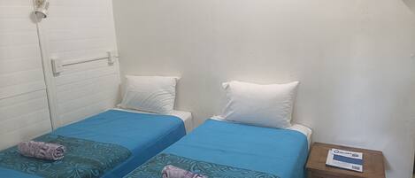 A small, clean room with two beds, a wooden nightstand, and a white door.