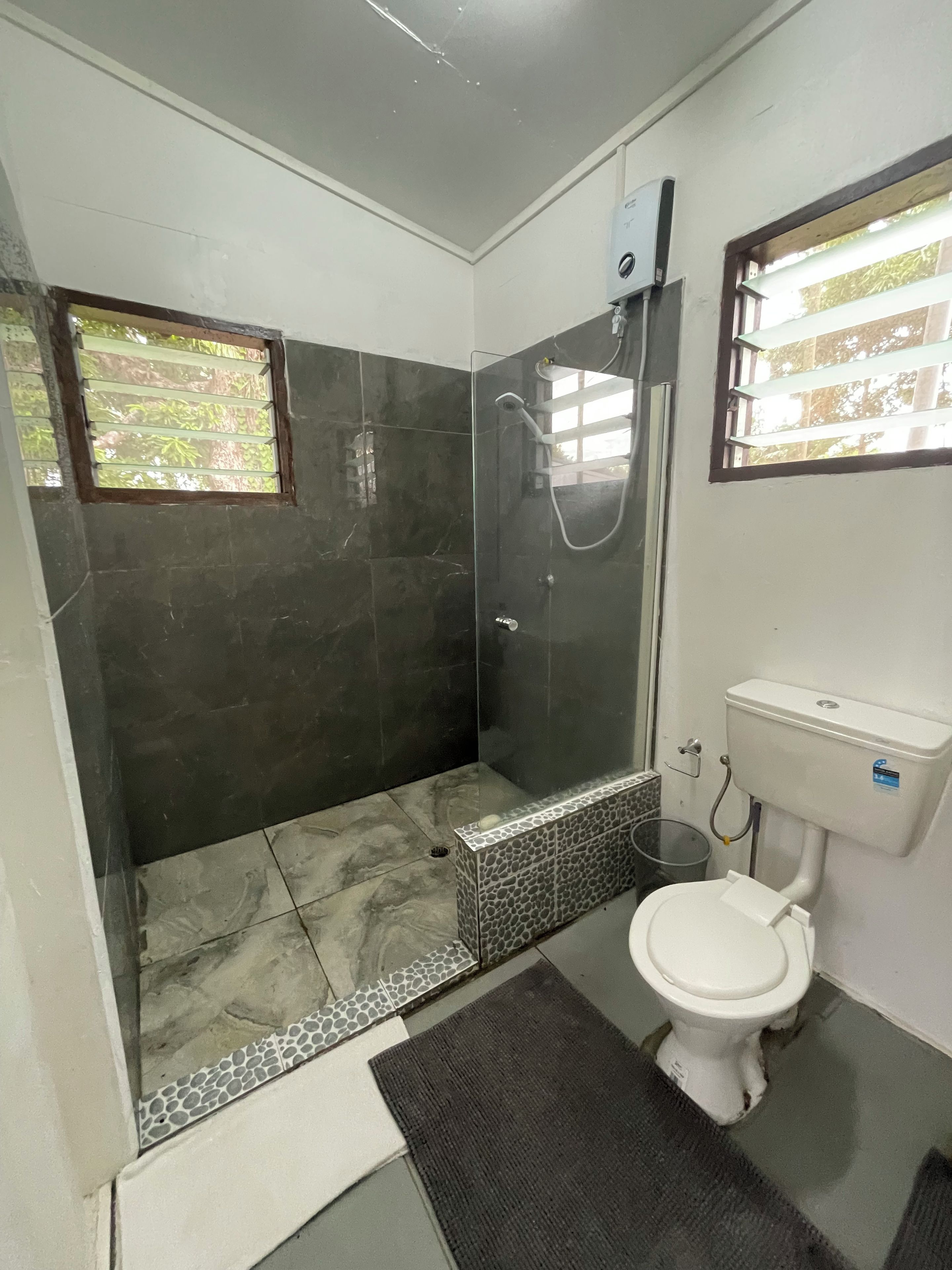 A bathroom with a shower, toilet, and a window.