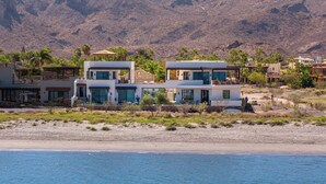 A coastal property with modern architecture, featuring multiple levels and balconies, situated by the beach with a mountainous backdrop. - Beachfront home & mountain views, and the biggest private pool (Loreto)