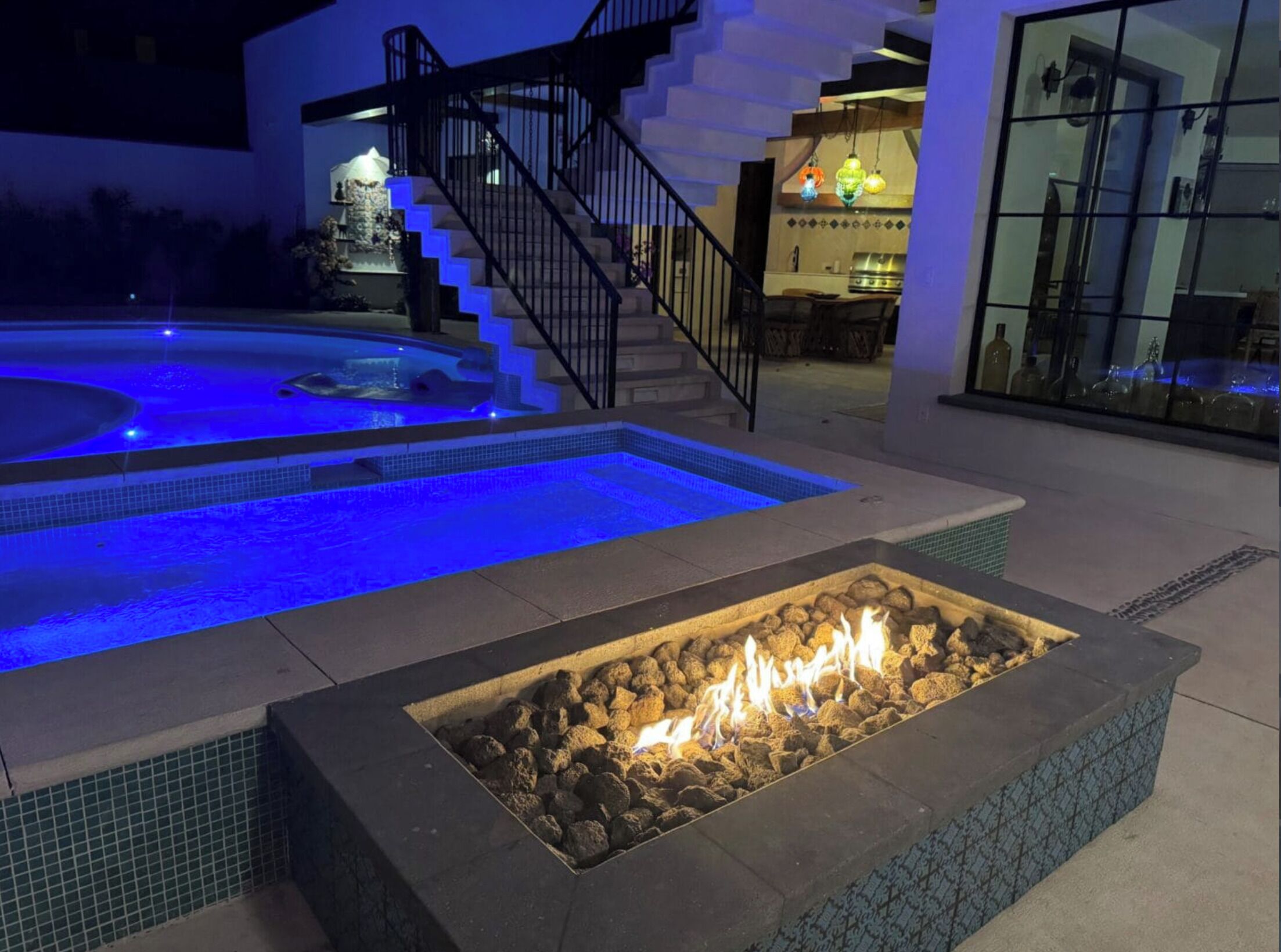 Une piscine éclairée de lumières bleues, un foyer extérieur et un escalier menant à un niveau supérieur.