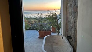 A bathroom with a bathtub, potted plants, and a view of the ocean at sunset. - Beachfront home & mountain views, and the biggest private pool (Loreto)