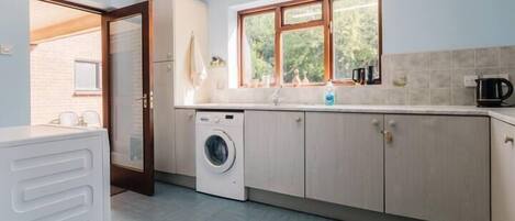 A laundry room with a washing machine, a sink, and a window with a view of greenery.