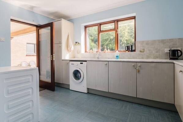 A laundry room with a washing machine, a sink, and a window with a view of greenery.