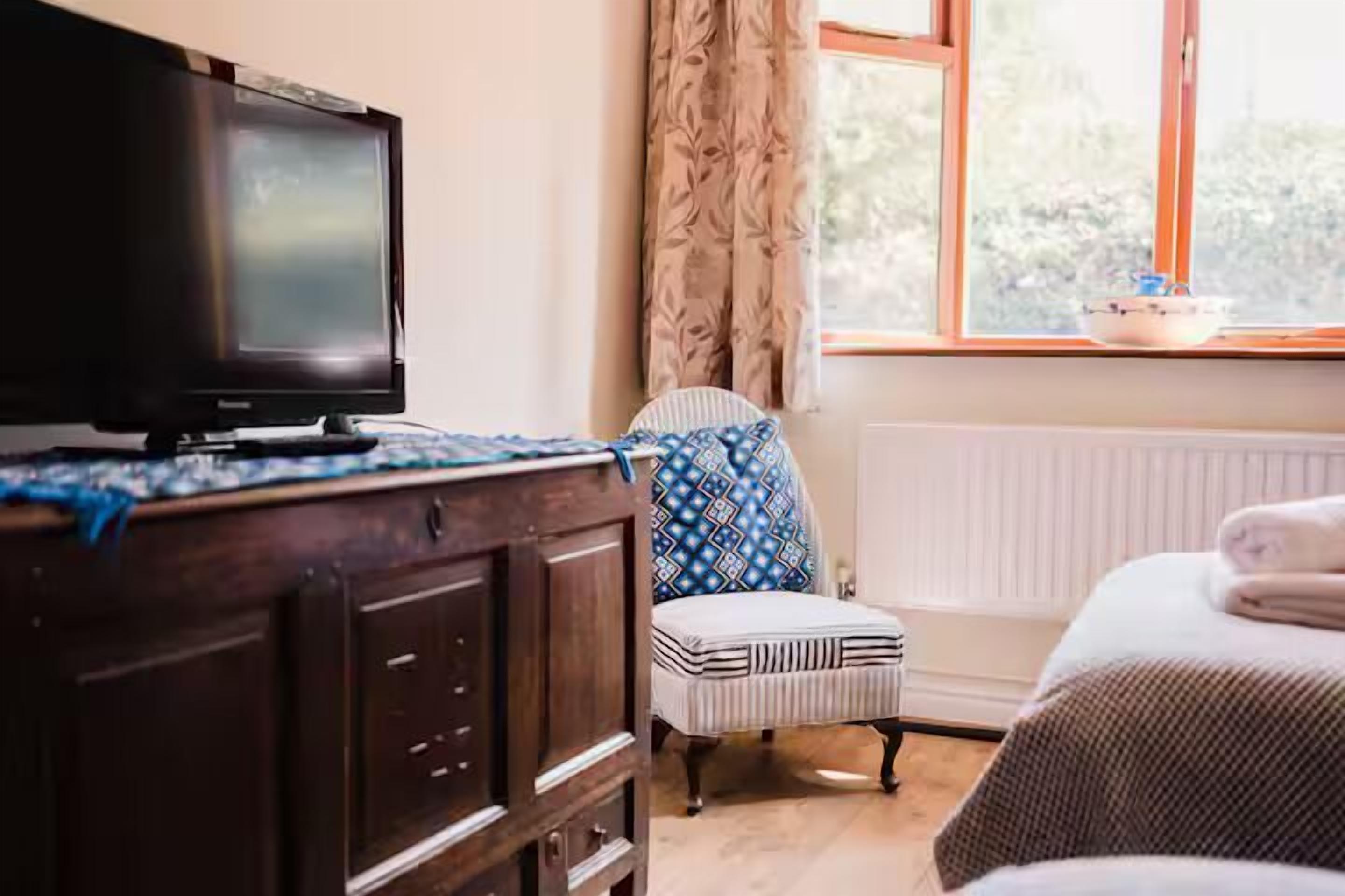 A bedroom with a bed, a chair, a dresser, a television, and a window with curtains.