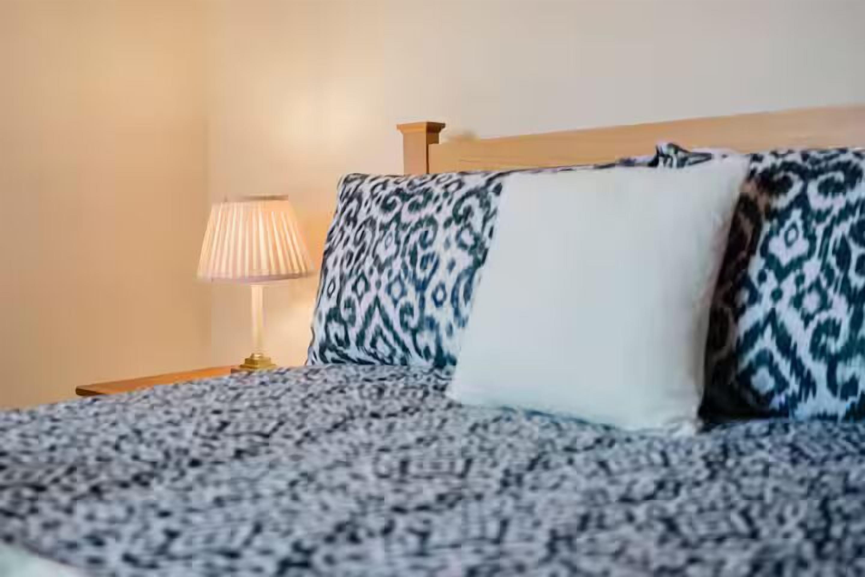 Un lit avec une literie et des oreillers à motifs, une lampe de chevet et une tête de lit en bois.