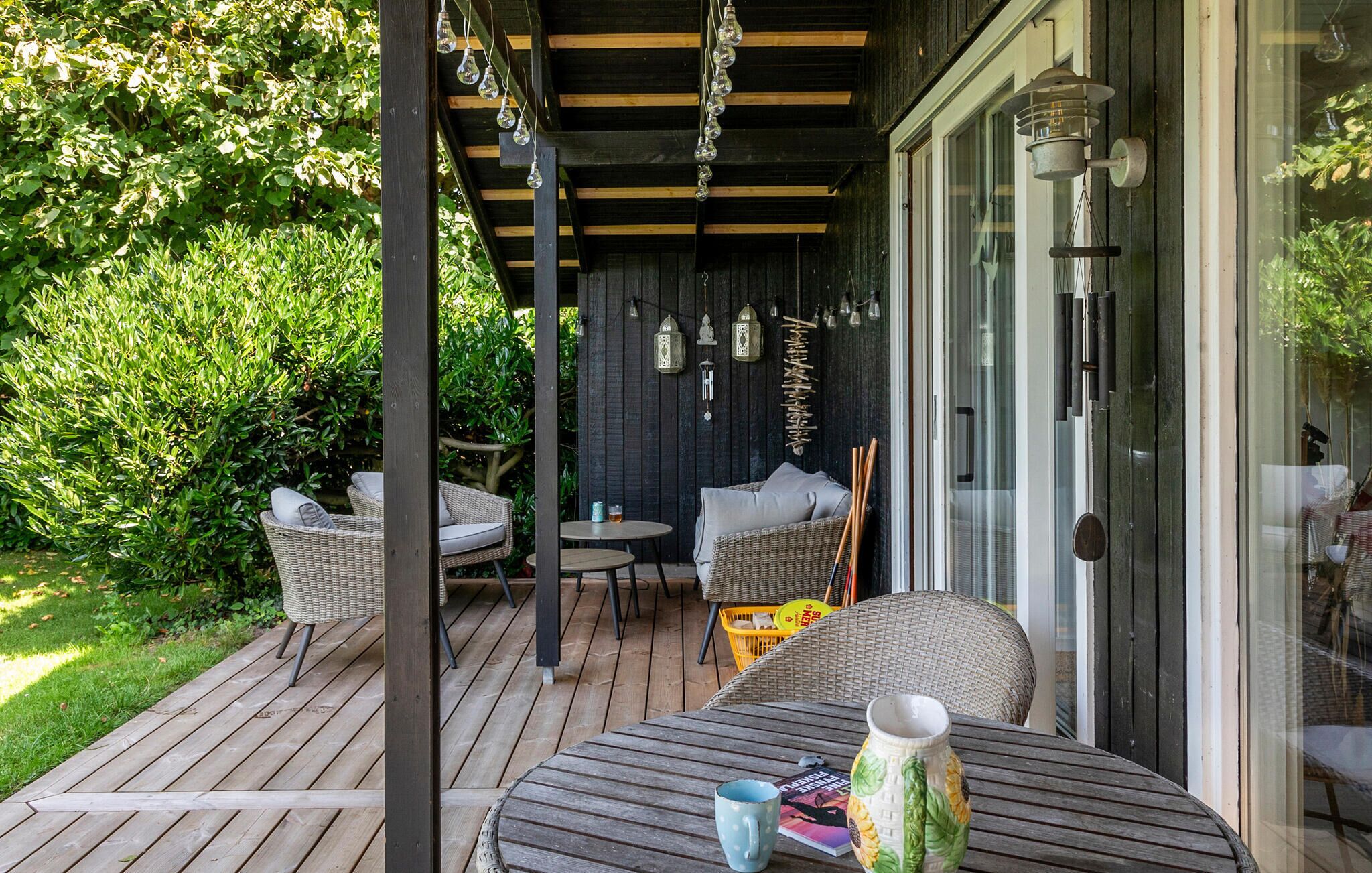 Eine überdachte Terrasse im Freien mit Korbmöbeln, einem Tisch und hängenden Leuchten.