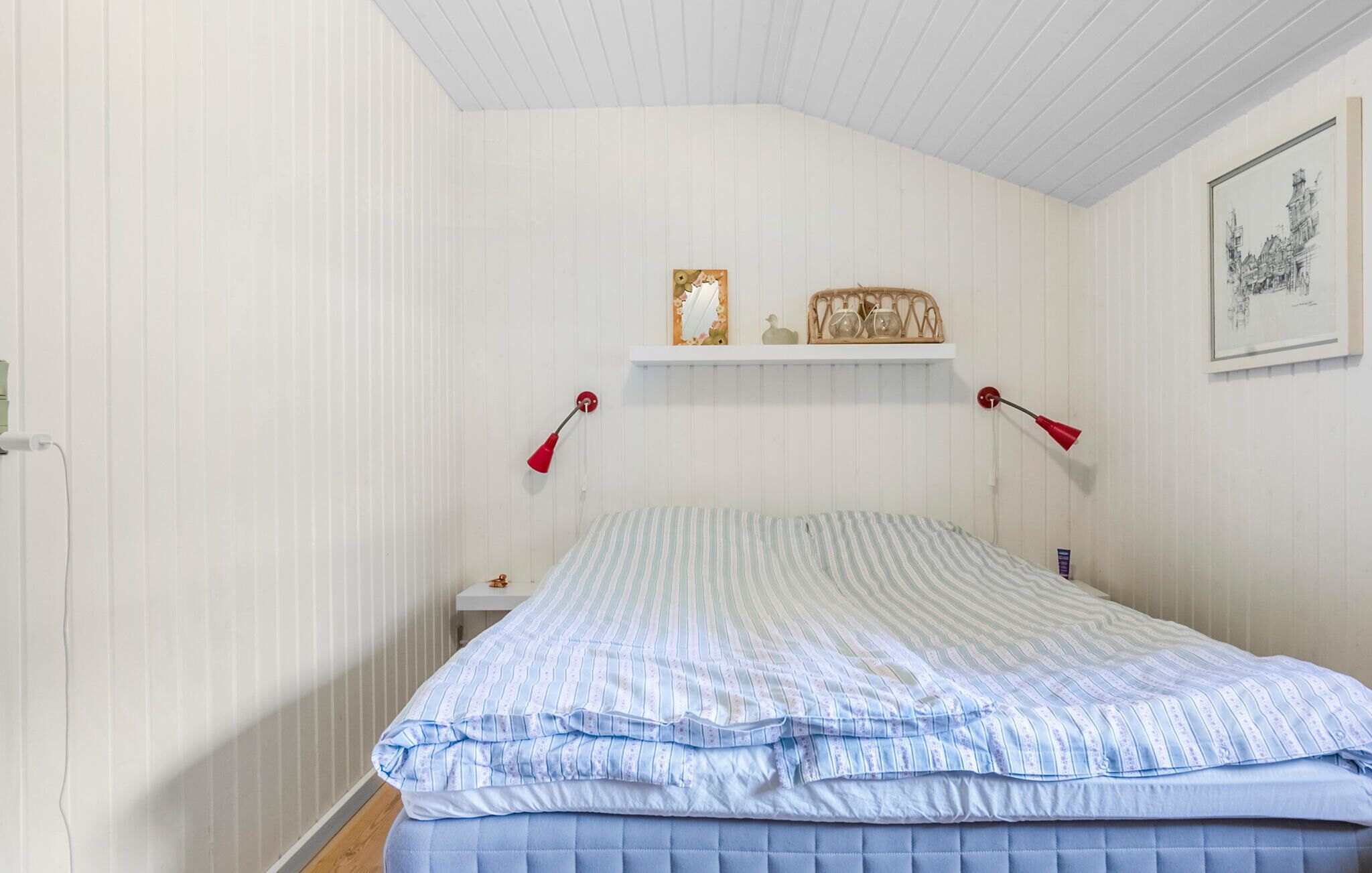 A bedroom with a bed, two bedside tables, a shelf with decorative items, and a framed picture on the wall.