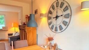Ein Essbereich mit Holztisch, einer großen Wanduhr und einer Vase mit getrockneten Ästen.