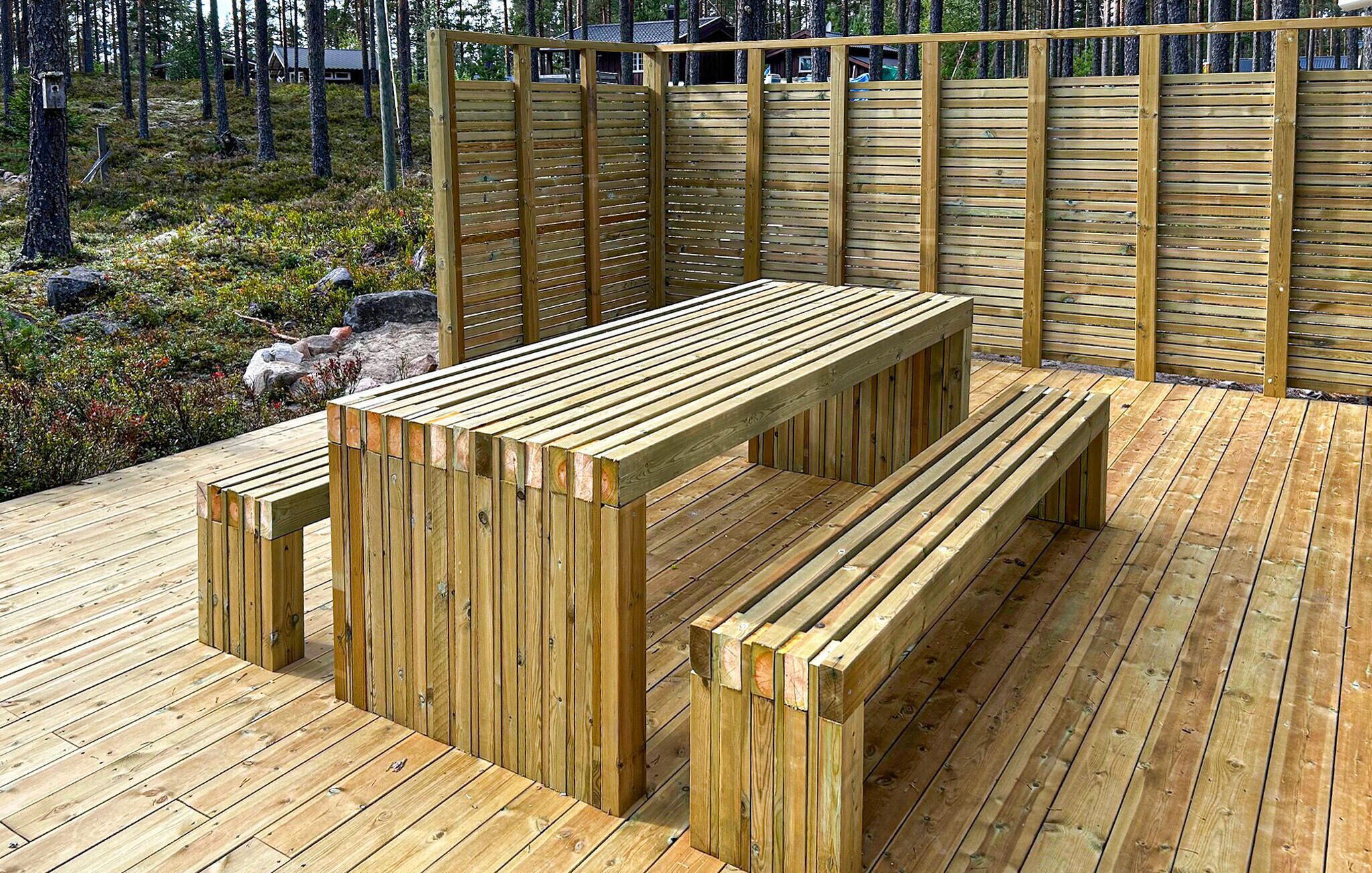 Une terrasse en bois avec un banc et une table, entourée d’une clôture en bois.