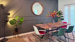 A modern dining area with a wooden table, green and red chairs, a large mirror, and a potted plant.