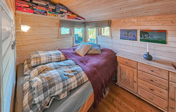 A cozy cabin bedroom with a bed, a dresser, and a shelf with books.