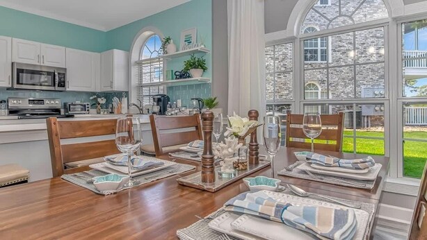 Comedor con mesa de madera para cuatro personas, electrodomésticos de cocina y vista a un edificio de piedra.