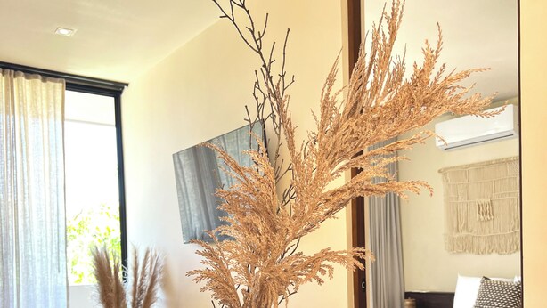 A dining table with a vase of dried plants, a sofa, and a bed in the background. - Peregrina Tulum 302B 1BR Condo (Tulum)
