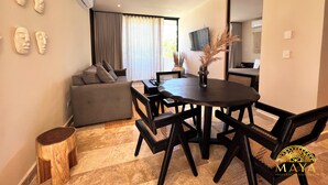 A modern living room with a sofa, dining table, and chairs. There are wall-mounted air conditioning units and a flat-screen TV. - Peregrina Tulum 302B 1BR Condo (Tulum)