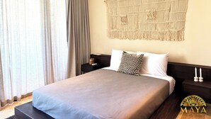 A hotel room with a bed, a nightstand, a macrame wall hanging, and an air conditioning unit. - Peregrina Tulum 302B 1BR Condo (Tulum)