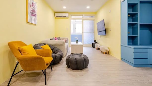 A living room with a sofa, armchair, ottoman, and a blue shelving unit.