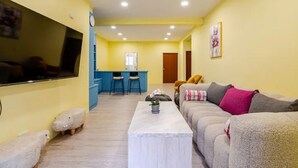 A living room with a sofa, a coffee table, and a TV. There is a kitchen area in the background.