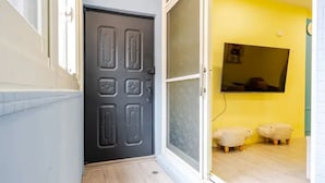 A hallway with a dark door, a glass door leading to a room with a yellow wall and a mounted TV.
