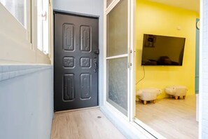A hallway with a dark door, a glass door leading to a room with a yellow wall and a mounted TV. - Luxurious Xinyi 101/City Hall MRT - Excellent location (Taipei City)