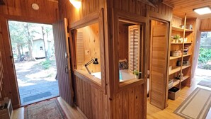 A wooden cabin interior with a kitchen area, a dining space, and a view of the outdoors.