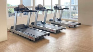 Un gimnasio con tres cintas de correr, ventanas amplias y suelo de madera.