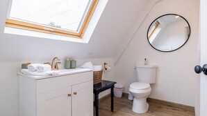 Een moderne badkamer met dakraam, witte inrichting, een zwart aanrecht en een ronde spiegel.