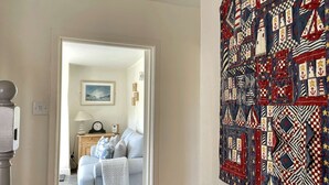 A room with a large nautical-themed quilt on the wall, a grey sofa, and a lamp on a side table. - A charming detached period cottage tucked into the town of Blakeney (Blakeney)