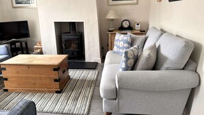 A living room with a sofa, wooden coffee table, and a fireplace. - A charming detached period cottage tucked into the town of Blakeney (Blakeney)