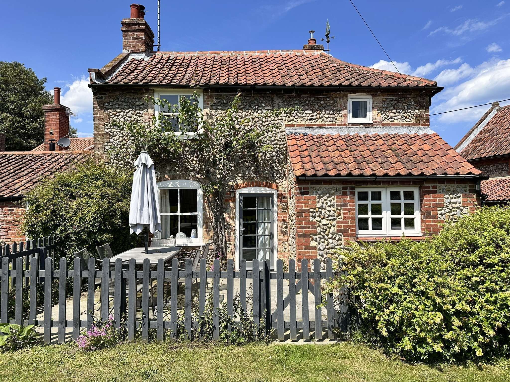 A stone house with a tiled roof, a wooden fence, and a garden.