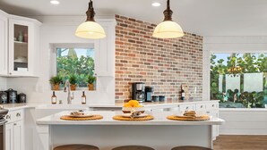 A modern kitchen with white cabinetry, a brick accent wall, and a large island with stools.