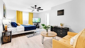 Une chambre d’hôtel moderne équipée d’un lit, d’une télévision, d’un ventilateur de plafond, d’un canapé, d’une table basse et d’un meuble de rangement.