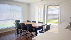 A modern kitchen with a white countertop, a sink, and a window overlooking a fenced yard. - Darcy Drive - All of the Comforts (Wagga Wagga)