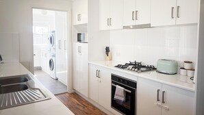 A modern kitchen with white cabinets, a stainless steel sink, a microwave, a gas stove, and an oven. - Darcy Drive - All of the Comforts (Wagga Wagga)