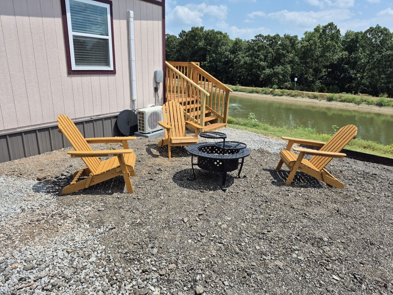 A gravel patio with Adirondack chairs, a fire pit, and a wooden deck leading to a building.