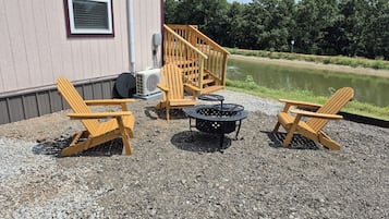 A gravel patio with Adirondack chairs, a fire pit, and a wooden deck leading to a building.