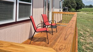 A residential building with a wooden deck, two red chairs, and a wooden railing. - RT66 Retreat Tiny Home (Big Cabin)