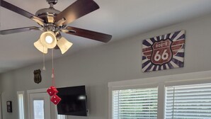 A room with a ceiling fan, a television, a Route 66 sign, and a bean bag chair. - RT66 Retreat Tiny Home (Big Cabin)