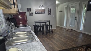A kitchen with a marble countertop, stainless steel sink, and a red refrigerator. There is a dining table with four chairs and a hanging light fixture above it. - Big Cabin Hideaway Tiny Home (Big Cabin)