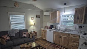 A compact living space with a sofa, coffee table, and a kitchen area including a stove, sink, and cabinets. - Big Cabin Hideaway Tiny Home (Big Cabin)