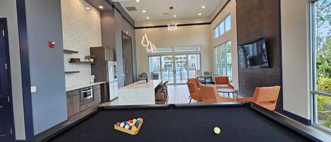 Un espace piscine moderne comprenant une table de billard, des sièges et une grande fenêtre donnant sur l’extérieur.