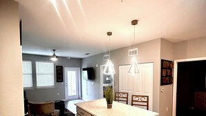 Une cuisine moderne dotée d’un grand îlot central, de planchers en bois, de luminaires suspendus et d’un coin repas agrémenté d’un tapis foncé.