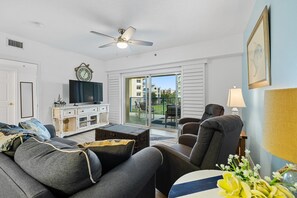 Una sala de estar con sofá, sillones, televisor y ventilador de techo.