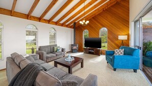 A spacious living room with a high wooden ceiling, a fireplace, a flat-screen TV, and comfortable seating.