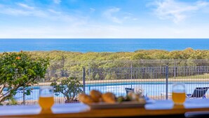 A poolside view with a clear view of the ocean and a fenced area with greenery.