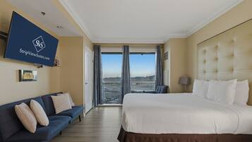 A hotel room with a large bed, a sofa, a TV mounted on the wall, and a view of a desert landscape.
